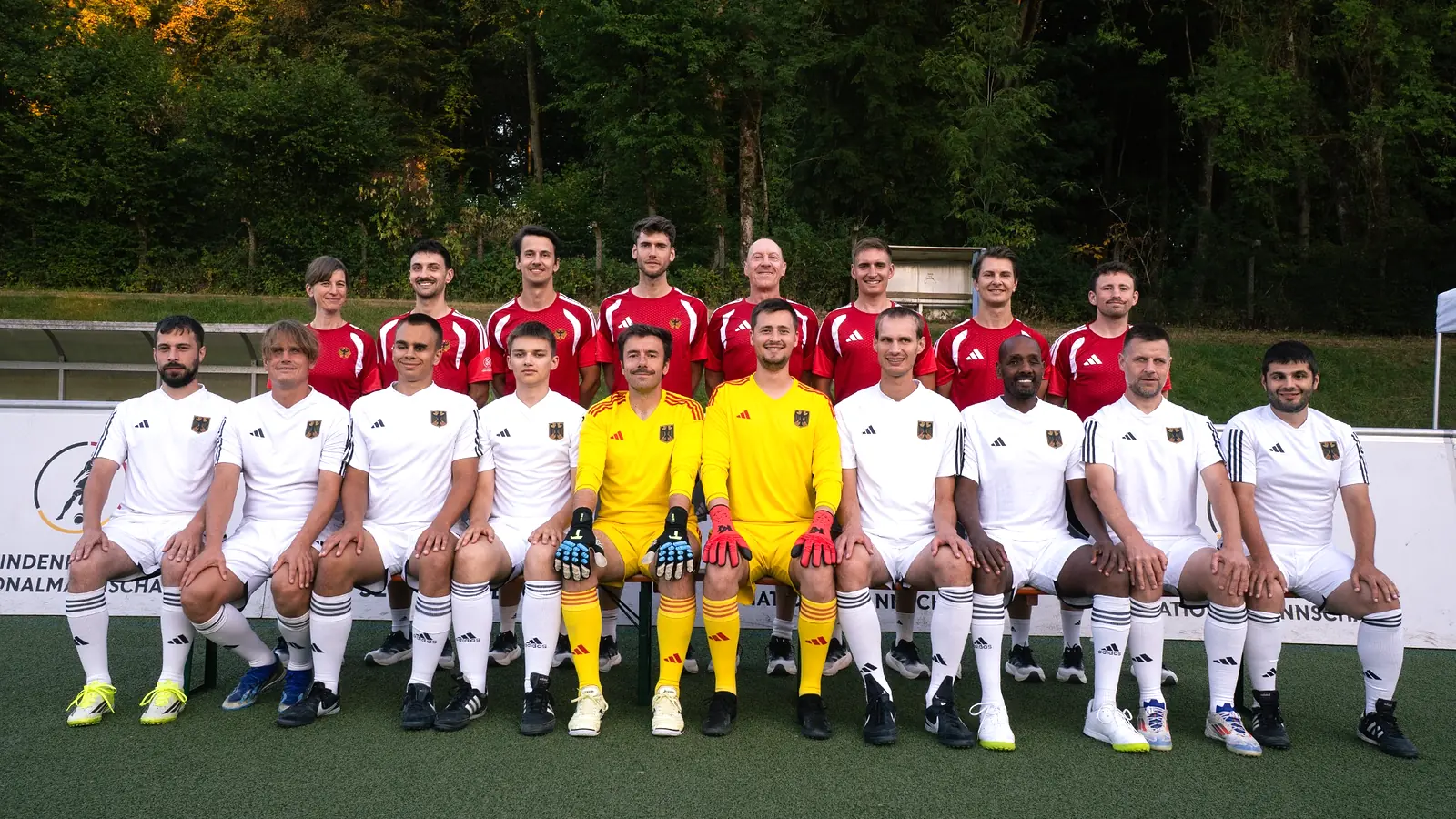 Die deutsche Blindenfußball-Nationalmannschaft mit Spielern in weißen Trikots, zwei Torhütern in Gelb und dem Funktionsteam in Rot beim Trainingslager in Grünberg.